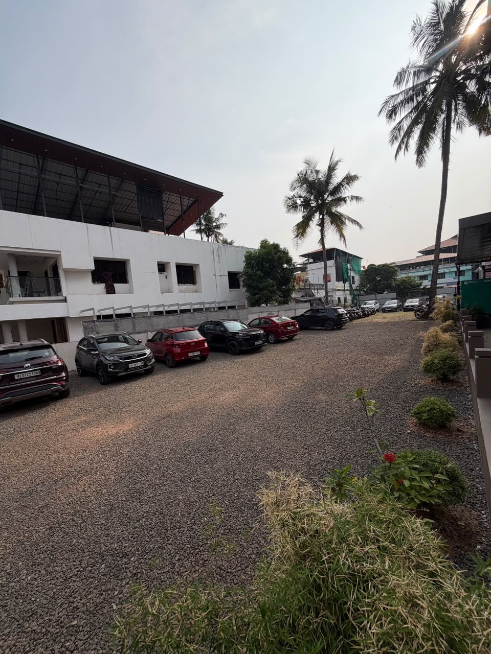 On-site car parking on gravel beside G K Tower, lined with plants and coconut palms